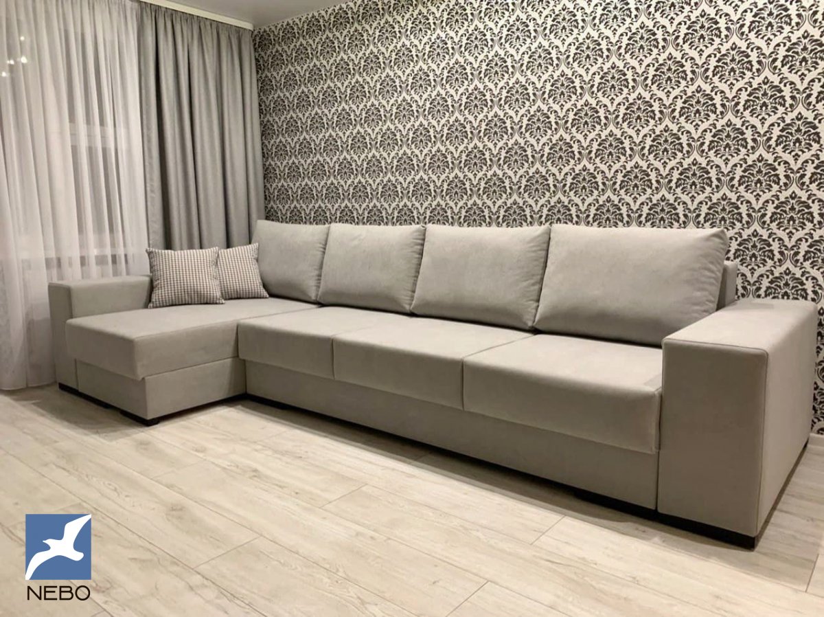 Большой раскладной диван в бежевой обивке с широкими подлокотниками и декоративными подушками в клетку