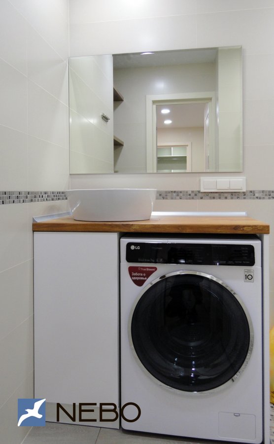 Белая напольная тумба в ванную с нишей под стиральную машину и распашным шкафчиком со столешницей из постформинга под дерево
