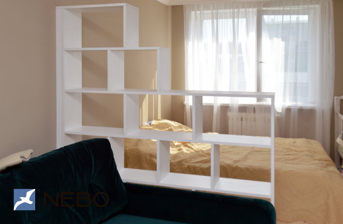 Белый зонирующий стеллаж из ЛДСП между спальным местом и зоной гостиной с диваном в однокомнатной квартире
