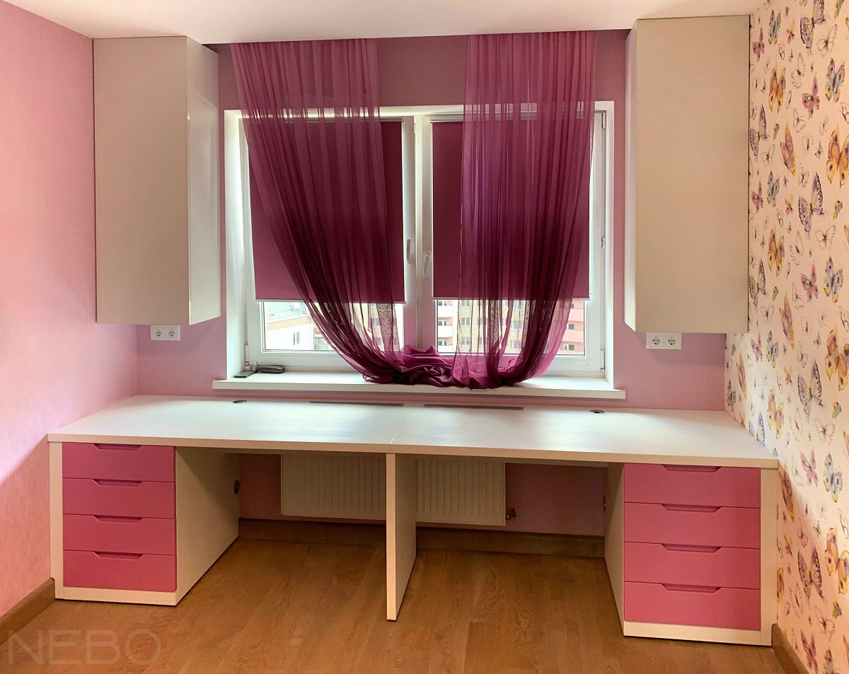 Компьютерный и письменный стол с розовыми фасадами у окна в комнату для двух девочек-школьниц