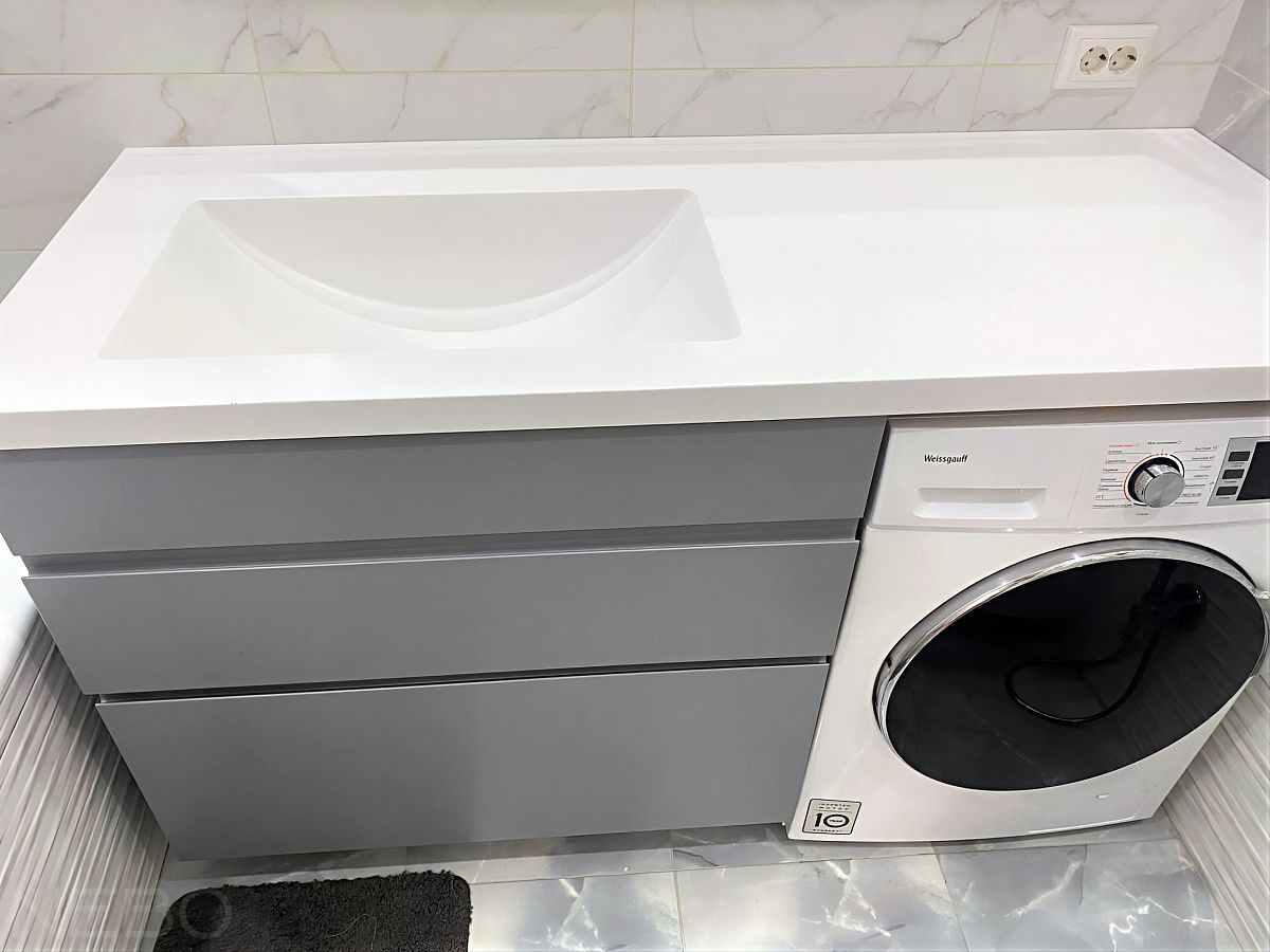 Серая напольная тумба с выдвижными ящиками возле стиральной машины под установку столешницы из камня