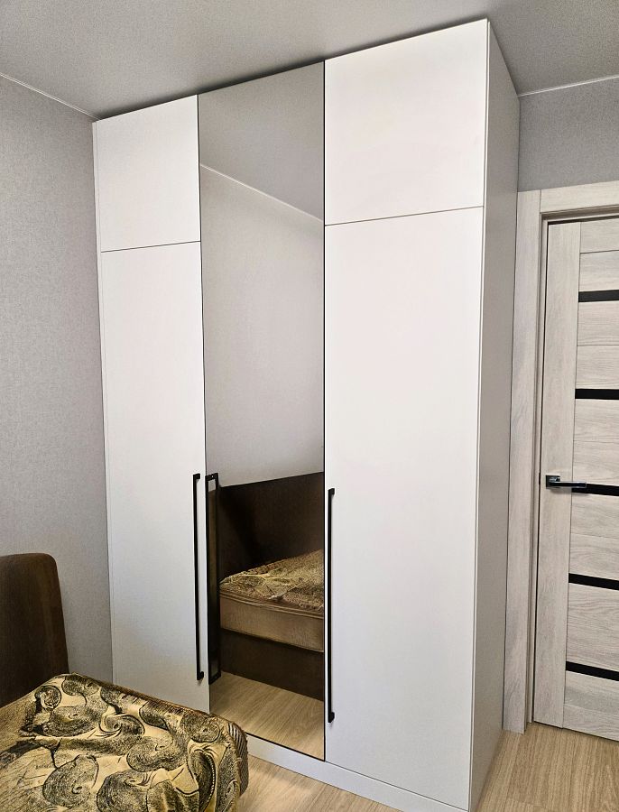 Белый трехдверный шкаф до потолка с зеркальной дверью по центру и длинными черными ручками