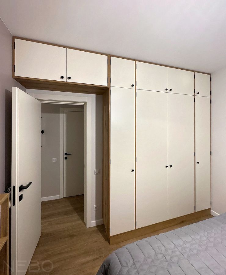 Узкий шкаф во всю стену с антресолью над межкомнатной дверью в спальне
