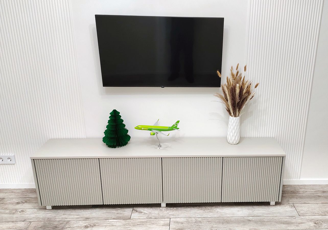 Серая тумба под телевизор с рифлеными фасадам на белых ножках в гостиную