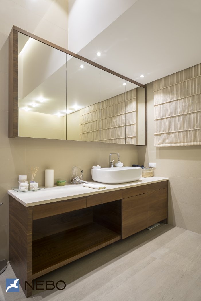 Мебель с отделкой шпоном для просторной ванной в частном доме с длинной напольной тумбой и навесными шкафчиками с зеркальными фасадами