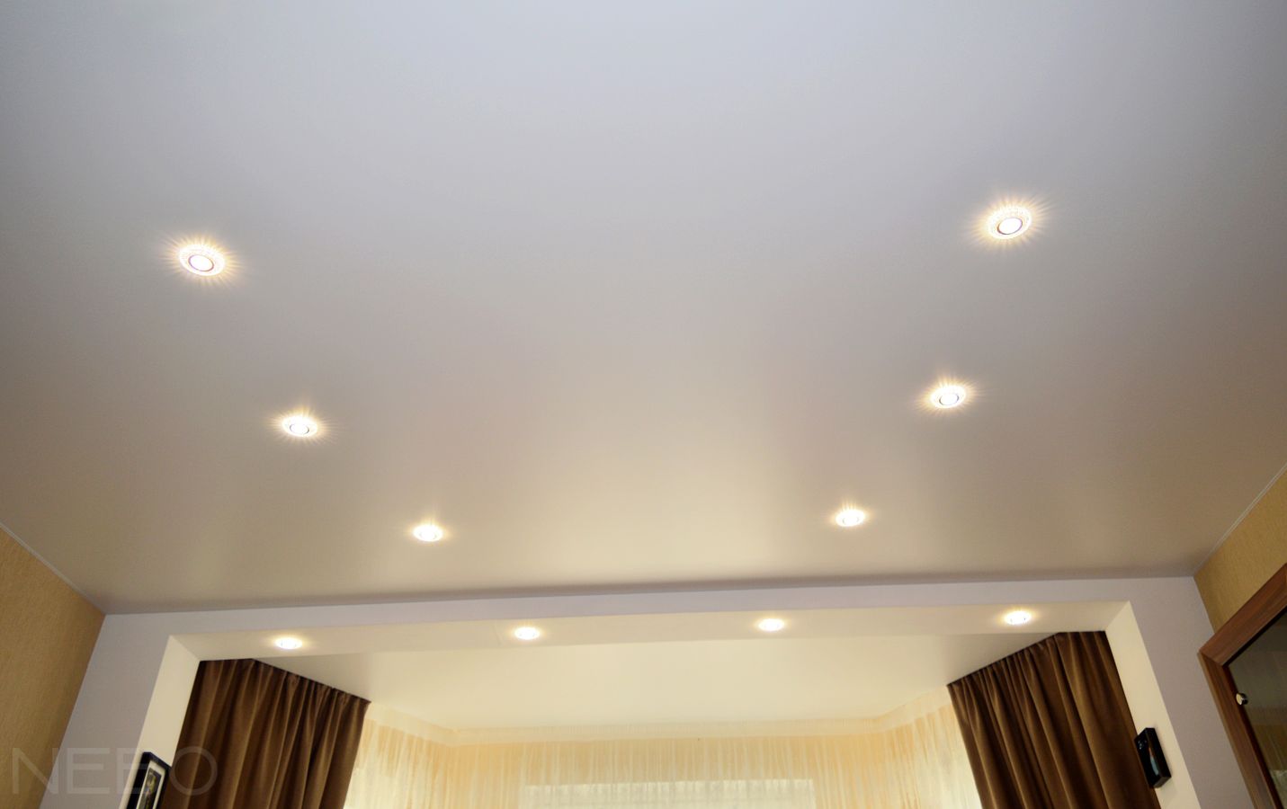 Белый натяжной потолок с трапециевидным участком у окна с нишами под карниз